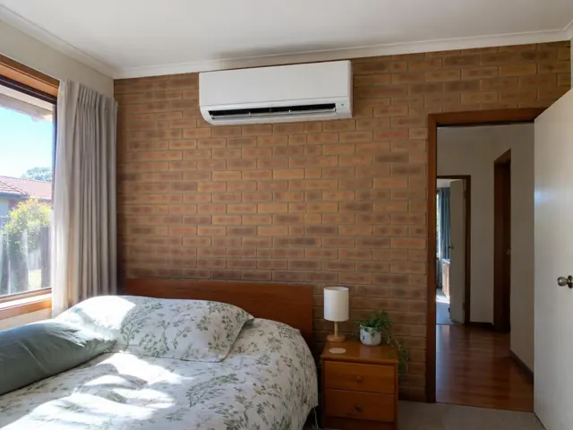 Split system mounted high on a brick bedroom wall above a bed, with louvre open in Elizabeth East