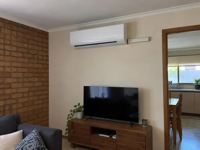 Wall-mounted split system above a TV in a brick-and-plaster living room in Elizabeth Vale